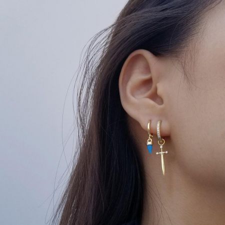 Design alternativi di orecchini che includono un ciondolo a forma di pugnale blu e un ciondolo a forma di pugnale d'oro.