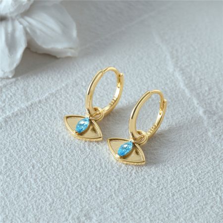 Un paio di orecchini huggie in oro con impostazioni di pietre blu triangolari.