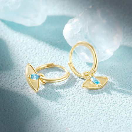 Scatto del prodotto degli orecchini huggie in oro con occhio maligno su uno sfondo semplice.