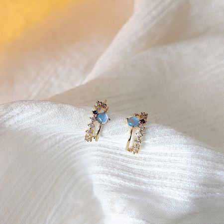 青い宝石と金の仕上げを強調したフレンチレトロスタッドピアスの詳細ショット。