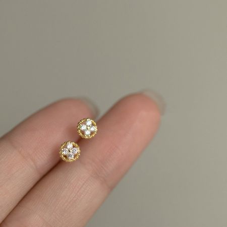 Gold version of the four-leaf clover stud earrings held between fingers to show scale.