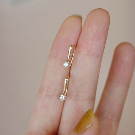 Detailed shot of the gold threader earrings held to display the zircon stones.