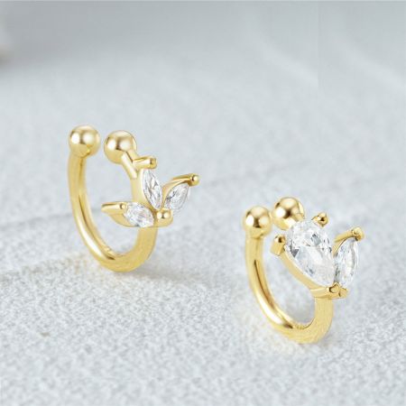 Vista dettagliata di un orecchino a clip in oro con un delicato design a foglia e gemme di zirconia trasparente.