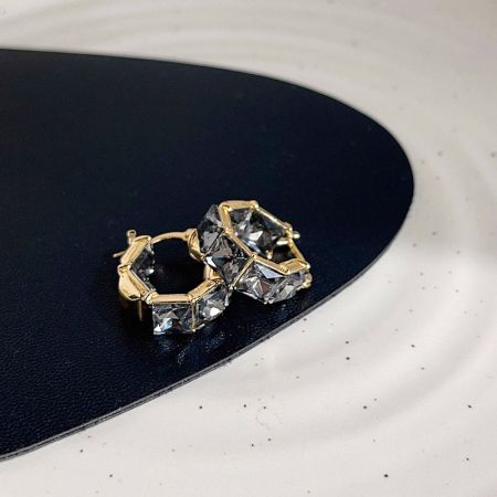 白い表面に展示されたクリアな宝石の金のイヤリングのペア。