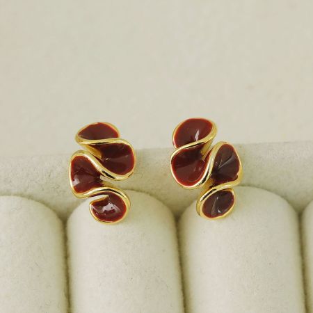 Los pendientes geométricos de esmalte rojo oscuro que muestran el intrincado diseño de ola.