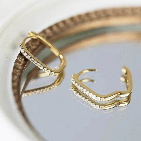 Un paio di orecchini huggie rettangolari in oro con brillanti accenti di diamante su uno sfondo bianco.