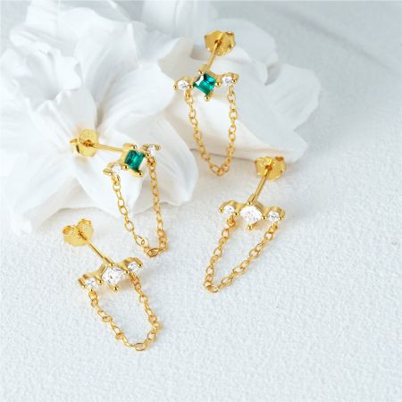 Eleganti orecchini dorati con catene pendenti, disponibili con pietre preziose verdi e chiare scintillanti.