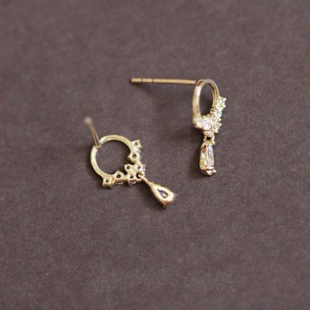 A pair of gold-plated teardrop earrings with white zircon gemstones, highlighting the intricate charm design.