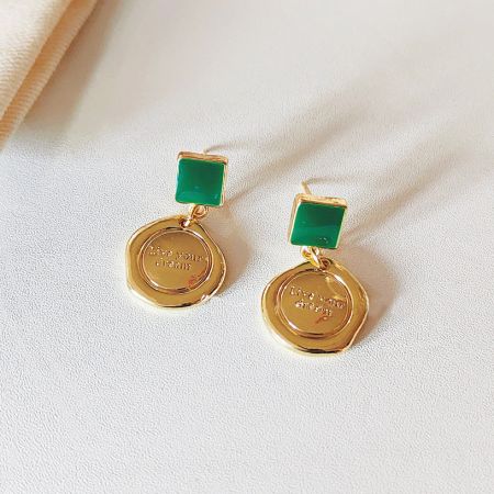 Profil latéral des boucles d'oreilles pendantes en émail doré et vert.