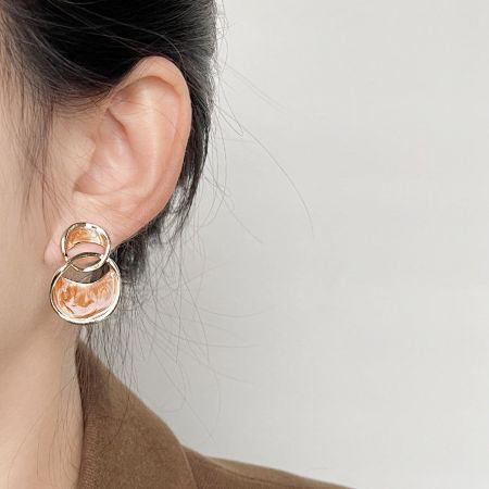 Une paire de boucles d'oreilles plaquées or avec un design unique à deux cercles et un émail marbré camel.