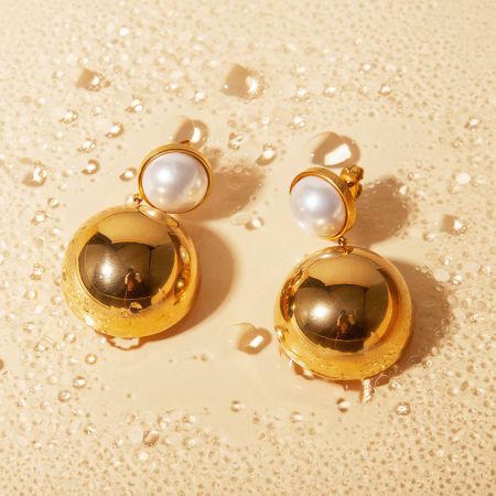 Un par de pendientes de cúpula hemisférica de oro con detalles de perlas exhibidos claramente.