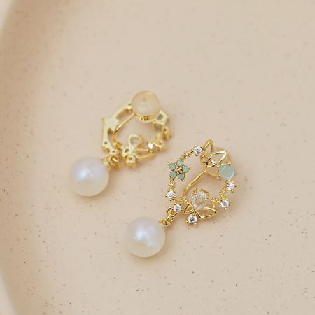 金のイヤリングの詳細なビューで、複雑な花柄と光沢のある白い真珠が強調されています。