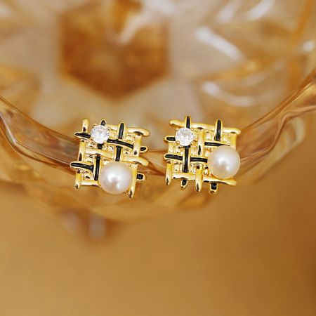 Detailed view of the braided mesh stud earrings with black enamel accents and a central pearl.