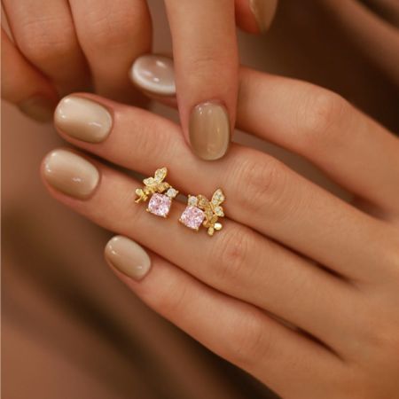 Close-up of the gold butterfly stud earring with a pink gemstone, worn on a hand to show scale.