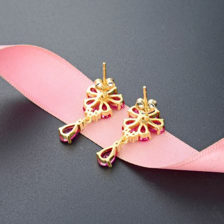 Vista dettagliata degli orecchini in argento sterling placcato oro, evidenziando il design floreale e la gemma rosa a forma di goccia.
