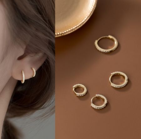 Orecchini huggie in argento sterling 925 di diverse dimensioni - Un paio di orecchini huggie in argento sterling 925 con finitura dorata lucida e pietre in zirconia cubica scintillanti, presentati su uno sfondo pulito.