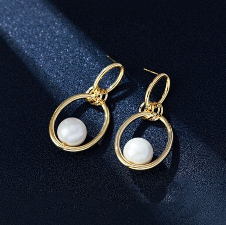 Gros plan détaillé de la bague ovale polie avec des boucles d'oreilles en perles mettant en avant la finition polie et la perle.