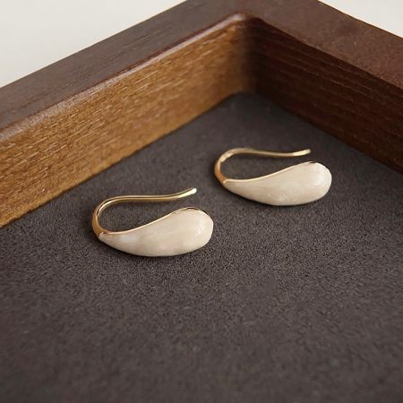 Vue rapprochée des boucles d'oreilles en forme de goutte d'eau plaquées or mettant en valeur la finition lisse de l'émail.