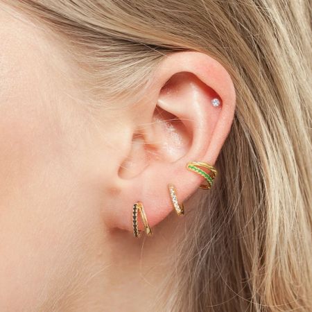 Modello che mostra un look a strati con vari orecchini a cerchio e a perno in oro.