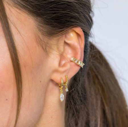 Vue rapprochée des trois boucles d'oreilles huggie en or sur l'oreille d'une femme.