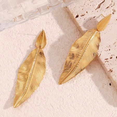 The gold feather earrings showcased on a textured pink stone.