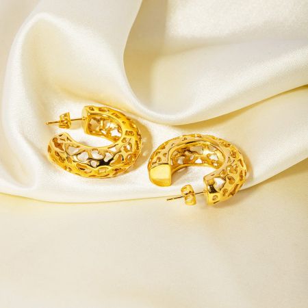 Los pendientes huecos en forma de C de oro grueso elegantemente exhibidos sobre una tela de satén crema para un toque lujoso.