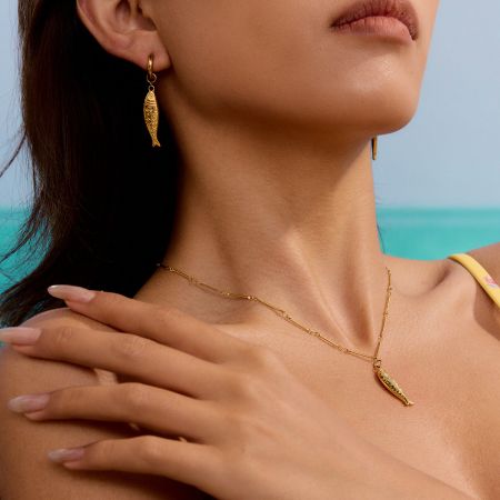 Collana con pendente a forma di pesce d'oro su uno sfondo di lino, che mostra il suo stile da spiaggia.