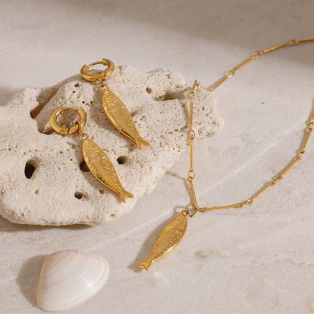 Ocean Beach Style Gold Fish Necklace and Earrings Set - A stunning gold fish-shaped jewelry set, including a necklace and earrings, elegantly displayed on a beige stone with a seashell, perfect for beach-themed styles.