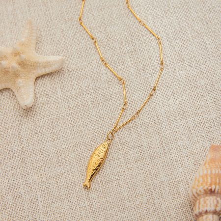 La collana con pendente a forma di pesce d'oro mostrata da vicino, enfatizzando la sua estetica a tema spiaggia.