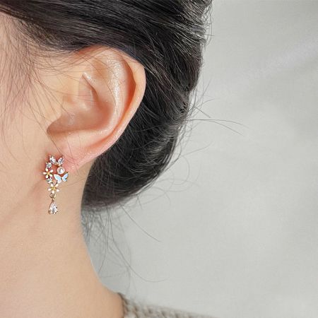 サイズと外観を示すために金の花の蝶のイヤリングを着用しているモデル。