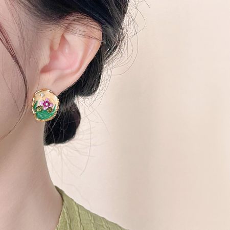 ピンクのエナメルの花と緑の葉をあしらった単一の金の花のイヤリングのクローズアップ。