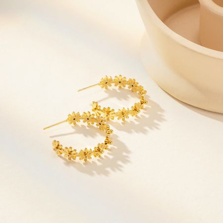Een volledig paar van de gouden bloemvormige C-vormige stud oorbellen, die hun symmetrisch ontwerp toont.
