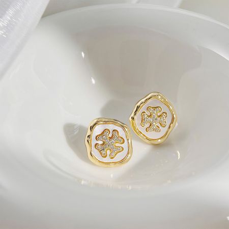 複雑な花のデザインと中央にクリアストーンがある金のイヤリングのペア。