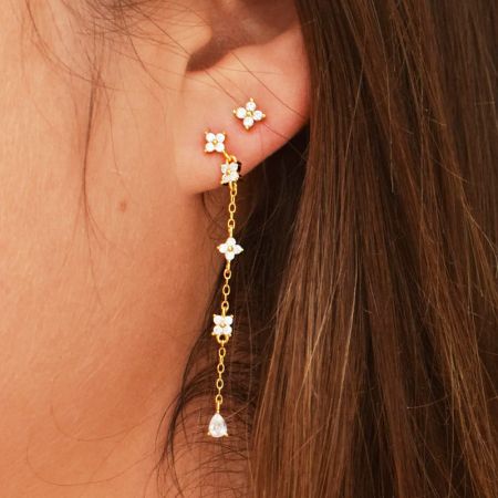 Un paio di orecchini floreali in oro con un elemento a cristallo pendente, esposti su uno sfondo bianco.