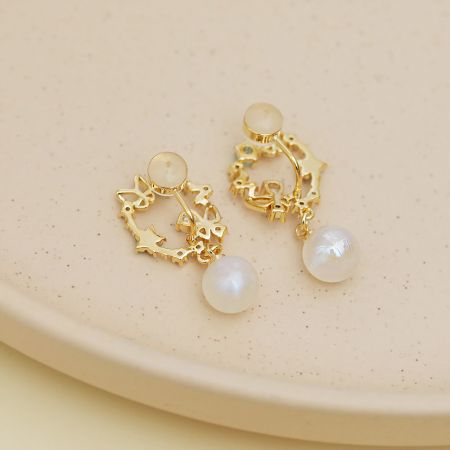 目を引く花柄デザインとクラシックな真珠のドロップが特徴のエレガントな金のイヤリングの全体像。