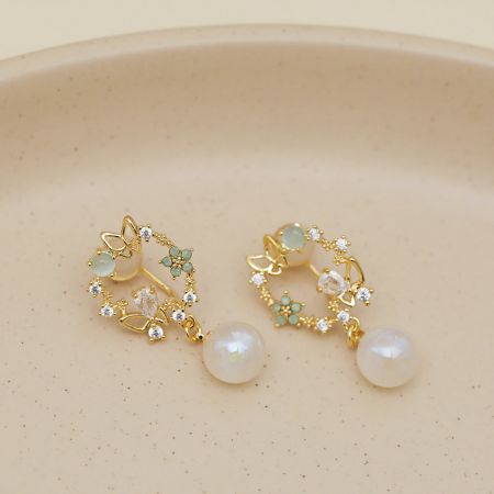 金の花柄イヤリングの別の角度で、きらめく透明なクリスタルと小さな緑の石が見えます。