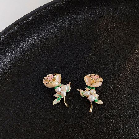 ピンクの花びら、白い真珠、金のベースに緑の葉があるフローラルイヤリングの詳細ショット。