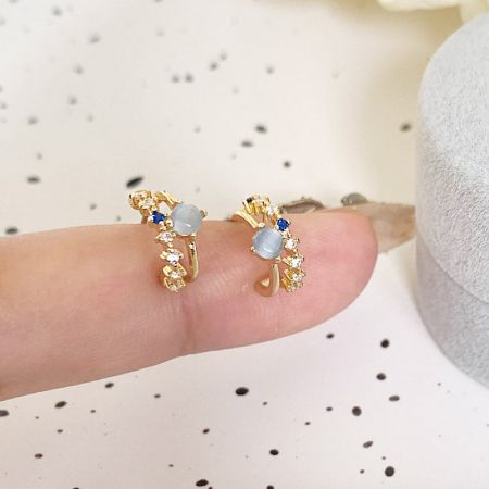 セットからの金の花柄デザインのイヤリングのペアで、繊細な白と青の石が特徴です。