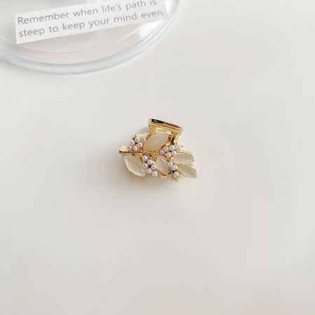 Close-up of a gold floral mini hair clip with a central pearl and rhinestone accents.