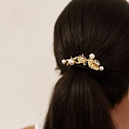 モデルがスリークなポニーテールで金色のヒトデのヘアタイを披露し、そのエレガントなルックを強調。