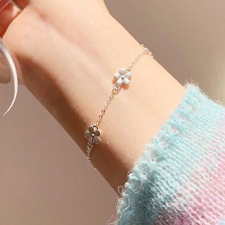 Primer plano de una pulsera de charm de flor chapada en oro del conjunto al por mayor en una muñeca.