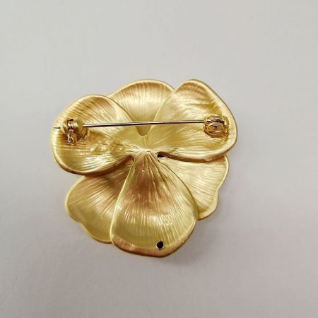 金色の花のブローチの背面ビューで、取り付け用の安全なピンクラスプを示しています。