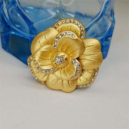 金色の椿の花のブローチの詳細なビューで、きらめくラインストーンを展示しています。
