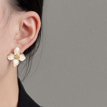 金メッキの白いエナメルの花のスタッドピアスを着用したモデル。