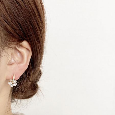 金色のジルコンクリスタルの花のスタッドイヤリングを着用している女性のクローズアップ。