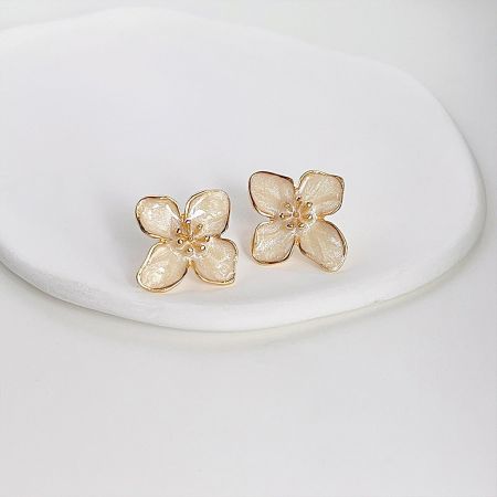 キラキラした白いエナメルの中心を強調した花のスタッドピアスのクローズアップ。