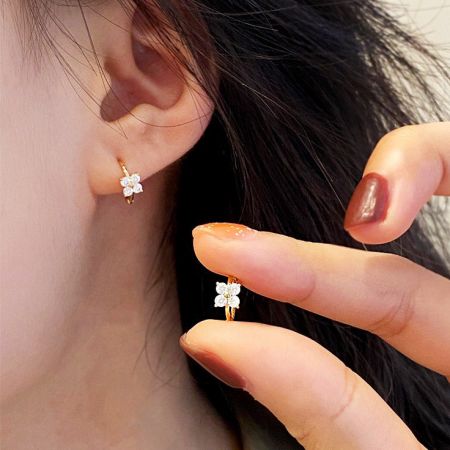 Mini 18K Vergulde Sterling Zilveren Klavertje Vier Hoepel Oorbellen - Een close-up van een vrouw die de mini 18K vergulde sterling zilveren hoepel oorbellen draagt en vasthoudt, met het delicate klavertje vier ontwerp met zircon stenen.