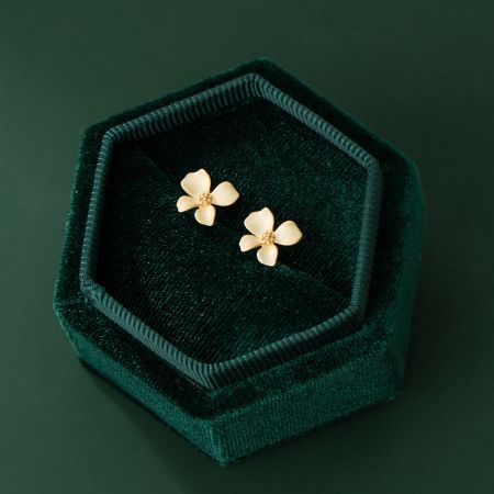 Orecchini a forma di fiore in oro elegantemente esposti in una lussuosa scatola di gioielli in velluto verde.