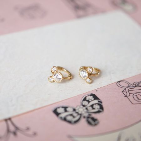 Foto do produto dos brincos huggie de prata esterlina com arranjo de pedras CZ em forma de flor em um fundo temático de borboleta rosa.