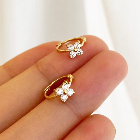 Een gedetailleerd uitzicht op de klavertje vier hoepel oorbellen die in de hand worden gehouden, met de sprankelende zircon stenen.